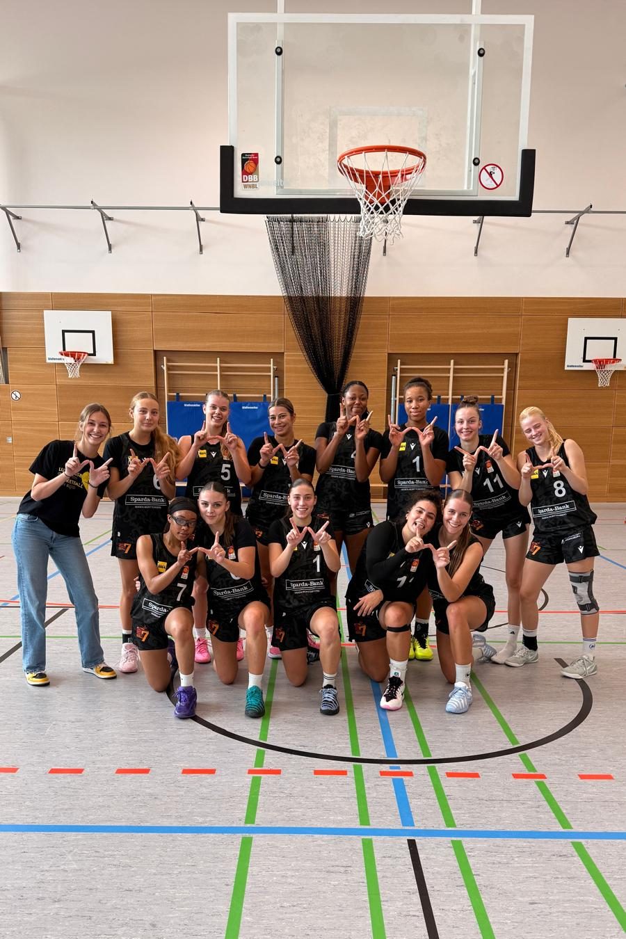 Die WNBL-Mannschaft nach dem Spiel unter dem Korb, alle formen mit den Händen ein W